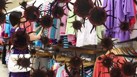 animation of macro covid-19 cells floating over caucasian woman shopping, looking through clothes