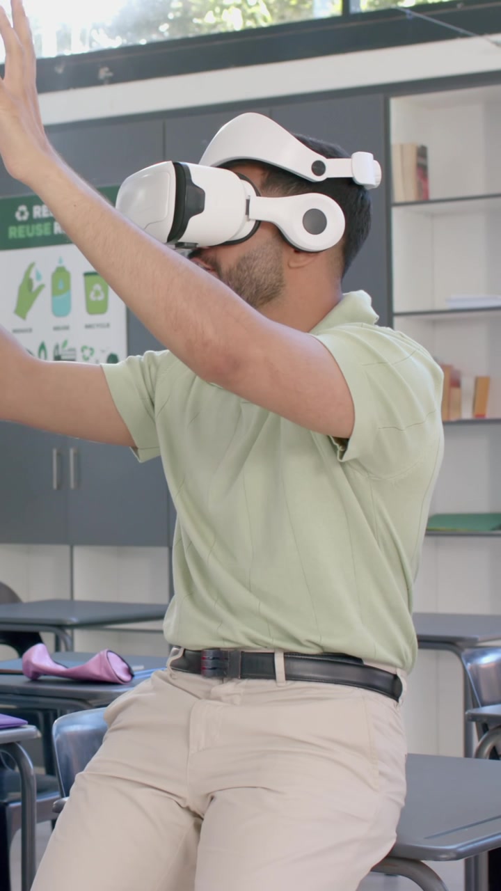 Video verticale: Insegnante indiano e ragazzo in classe che guardano l'insegnante indossare un visore VR e gesticolare.