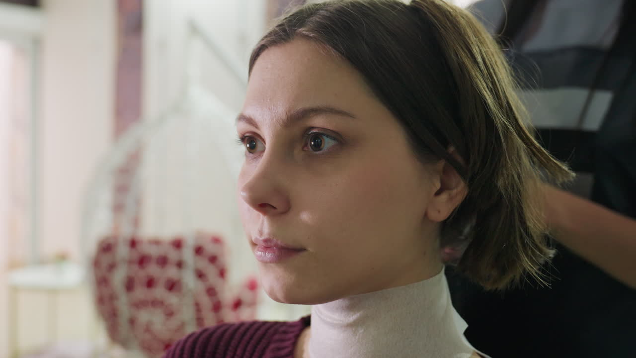 Primer plano del perfil de una mujer caucásica en un salón de belleza mientras la peinan durante el peinado final y el secado, con el estilista arreglándole el pelo, comprobando el resultado en el espejo y con expresión serena, iluminación moderna y cálida, capa