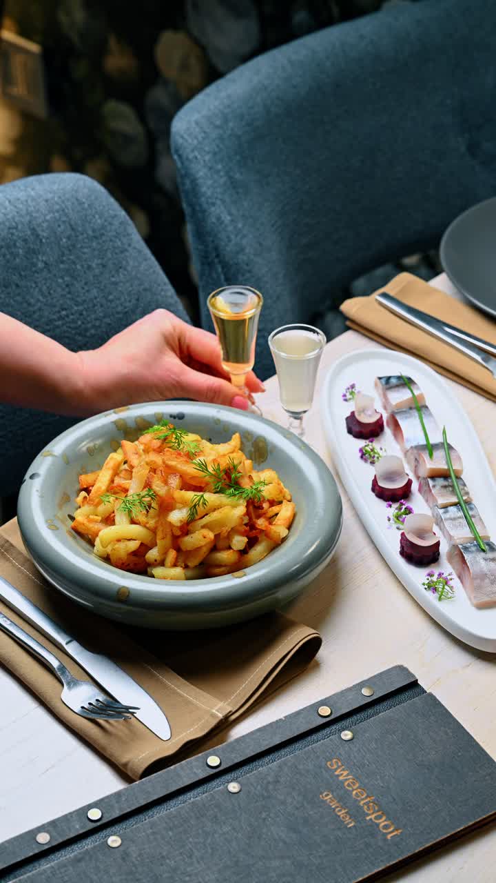 Mano che prende un bicchiere di liquido ambrato al ristorante. Una persona si allunga per afferrare un piccolo bicchiere di liquore o vodka aromatizzata su un tavolo con antipasti e cibo.