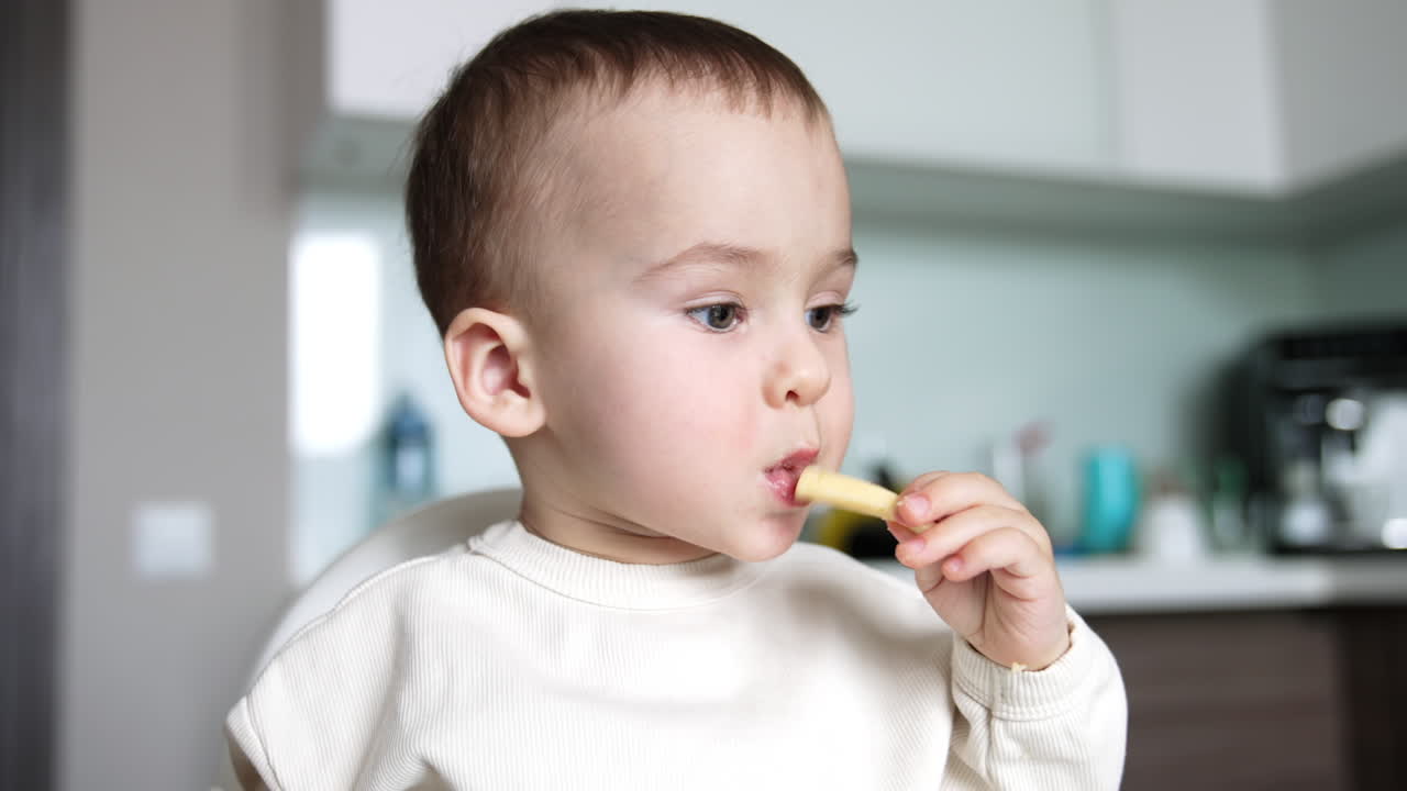 Beautiful child eating porridge from spoon. Cute little boy grabs a piece of cheese and takes a bite. Close up.