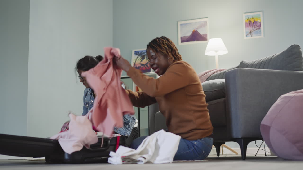 Excited ladies throw clothes into suitcase sitting on floor