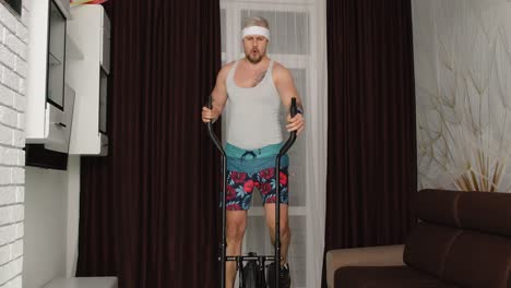 Sportsman-retro-guy-in-funny-clothes-making-sport-workout-fitness-cardio-exercises-on-orbitrek-home