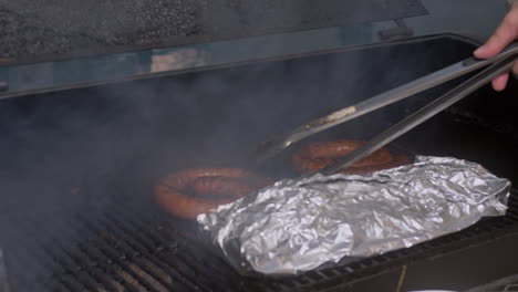 tilt down to tongs moving bbq sausage around on smoking bbq pit