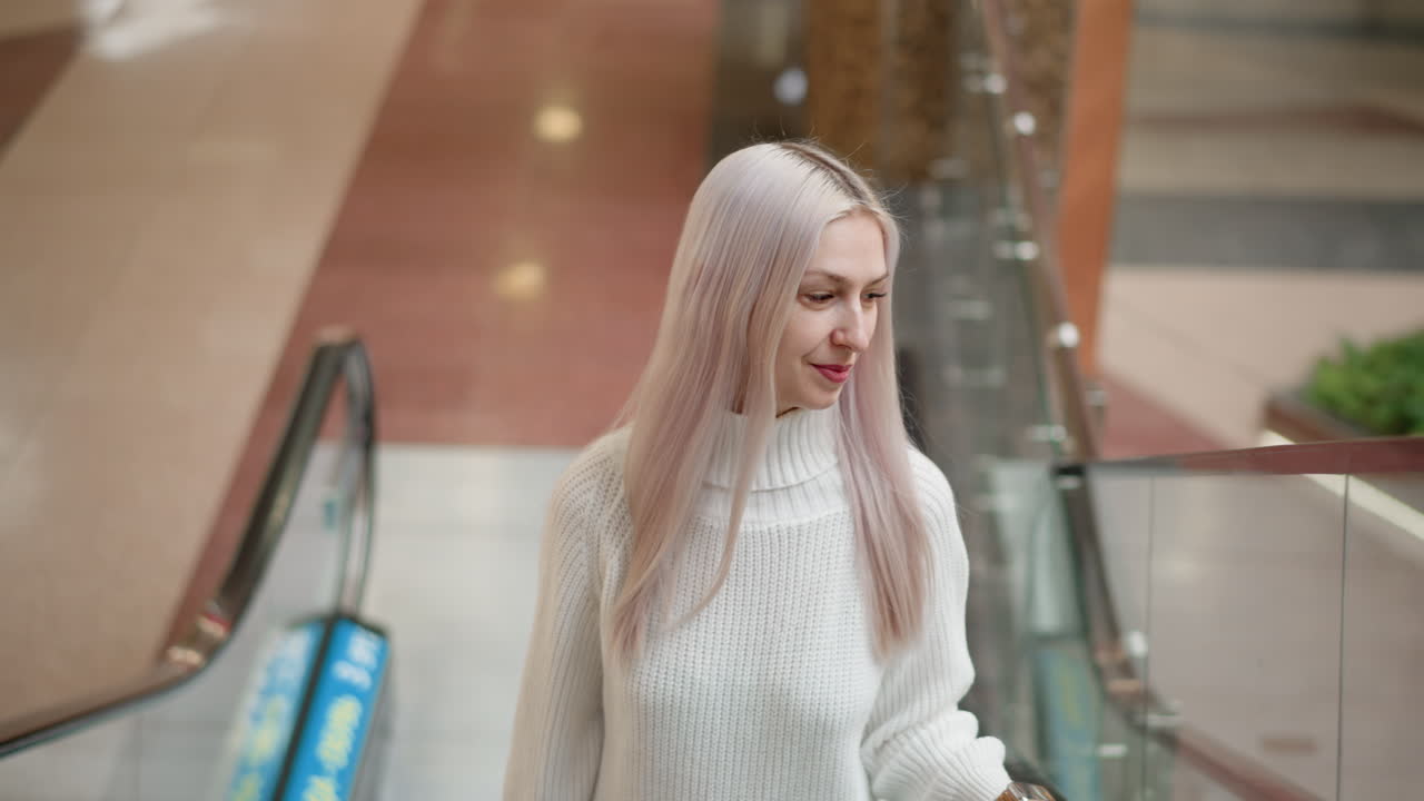 cheerful youthful lady on moving walkway looking sideways in admiration under bright mall lights beside glass railing on polished floor capturing casual elegance and dynamic motion