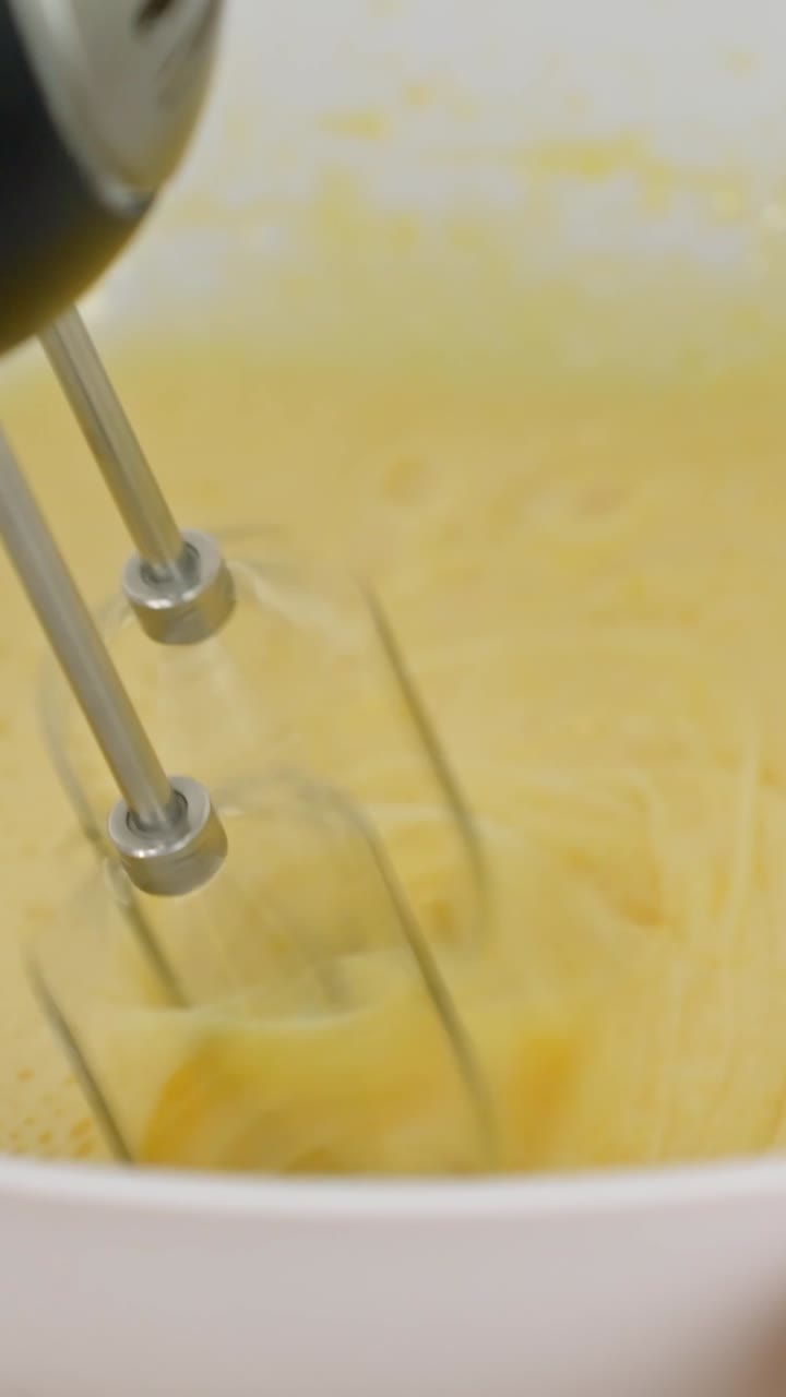 Close-up of an electric mixer whipping a yellow batter for a tiramisu cake