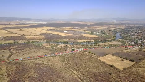 wide-aerial-side-view-of-several-train-wagons-on-a-railroad-track-passing-through-a-town-during-the-daytime