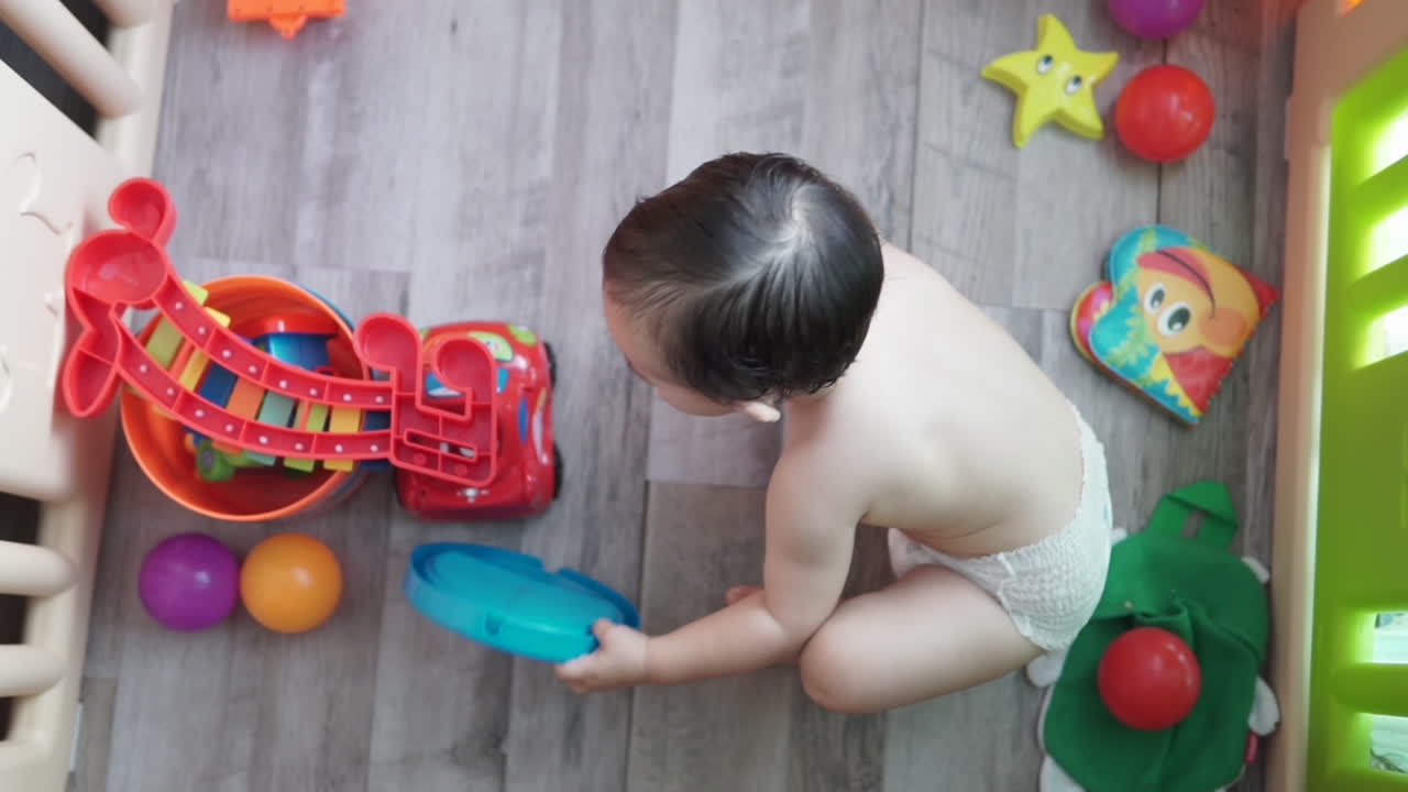 屋内の遊び場で自宅の床にカラフルなおもちゃで遊んでいる新世代の 1 歳のアジアの男の子のハイアングル ショット