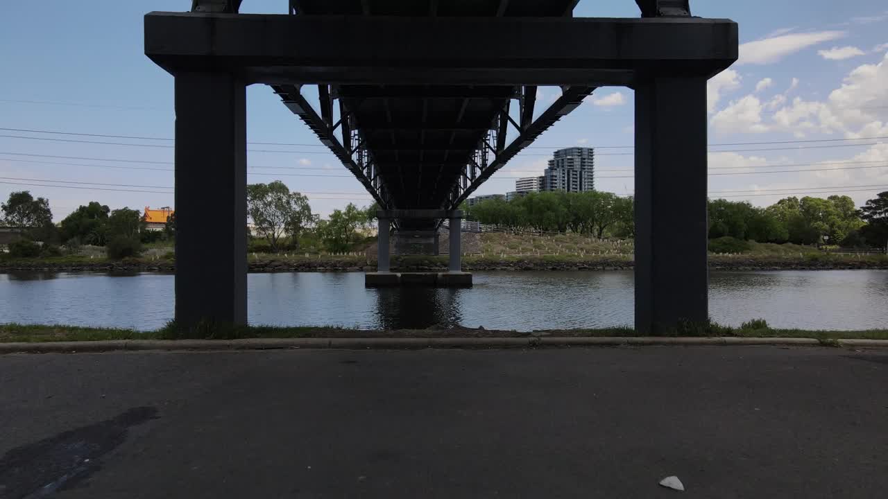 Aerial drone flies under bridge over river in Footscray, Melbourne, cinematic view