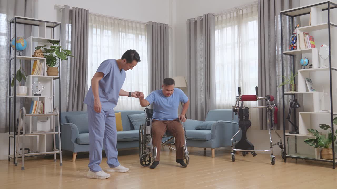 아시안 남성 간호사의 몸이 체어에 앉아있는 환자의 손을 들고 집에서 물리 치료 중에 일어서서 고 있습니다.