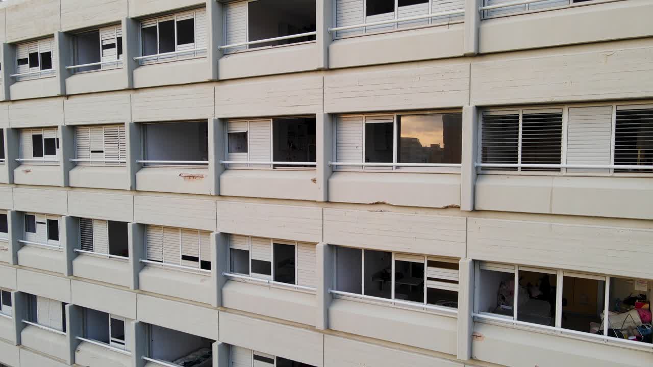 Drone close-up, shattered windows, residential building, Tel Aviv, missile aftermath, structural damage, broken glass, facade, balconies, interior visible, urban area