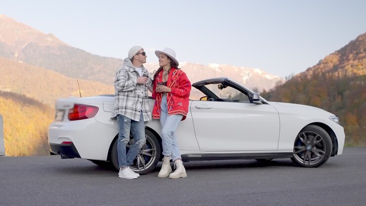 Pareja disfrutando de una pausa para el café en un coche descapotable en una carretera de montaña