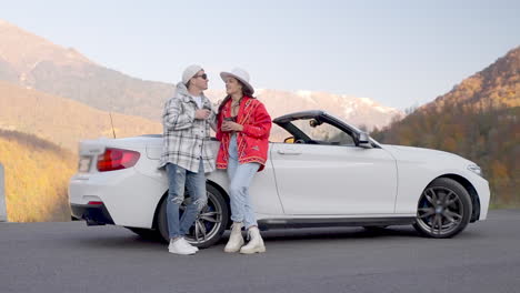 couple enjoying coffee break in convertible car on mountain road