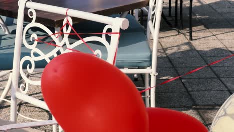 two red heart-shaped balloons tied to a chair are blown by the strong wind