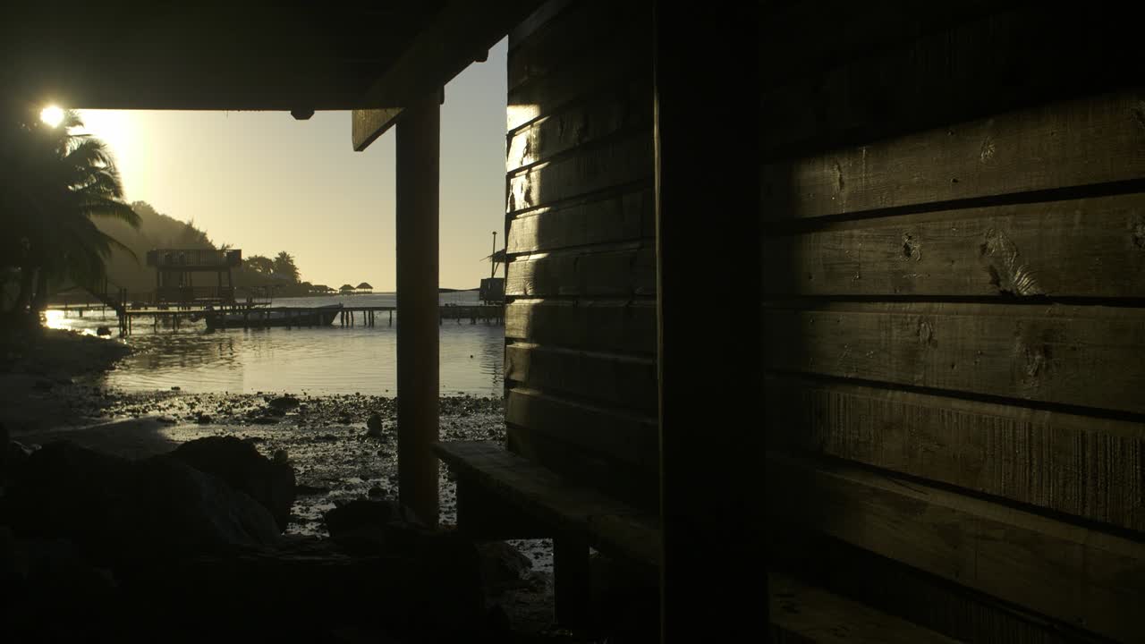 온두라스의 로아탄에 있는  ⁇ 타 고르다 해변은 해가 지는 동안 나무 기지 구조 아래에 있습니다.