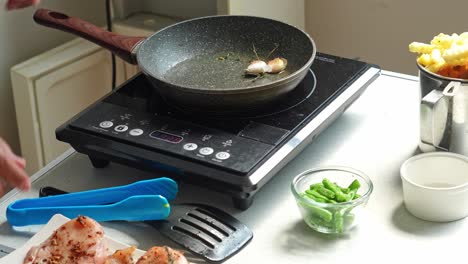 hands putting garlic into the pan to fry chicken steak