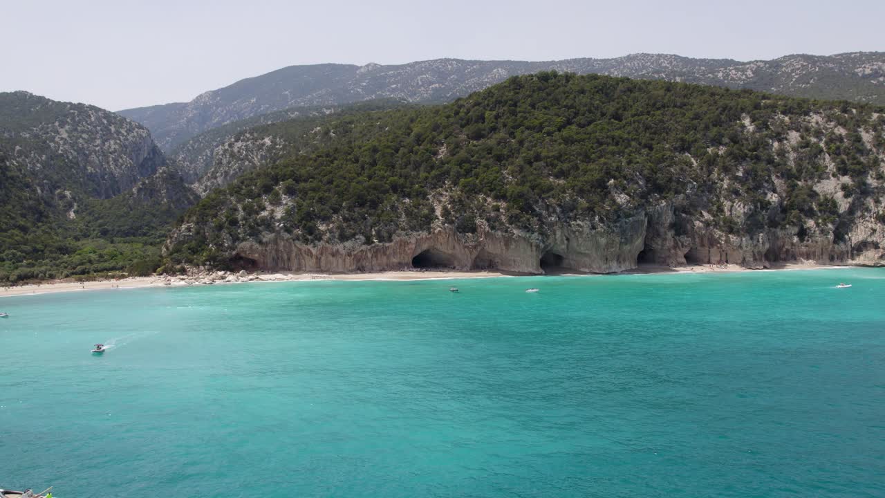 Scenic Turquoise Sea and Cave-Lined Beach with Mountains