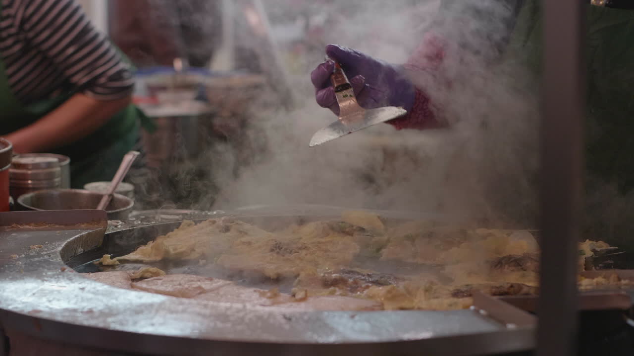 Street vendor in Taiwan at a popular night market fries oyster omelets and turnip cakes over a large fire. Slow motion footage.
