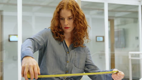 animación de formas rojas sobre mujer caucásica usando cinta métrica en la oficina