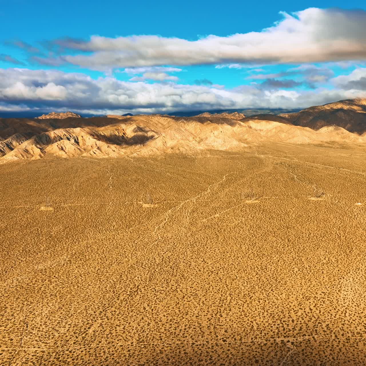 Plain deserted landscape surrounded by rocks. Beautiful blue sky with white clouds contrasting with yellow scenery of the desert. Top view