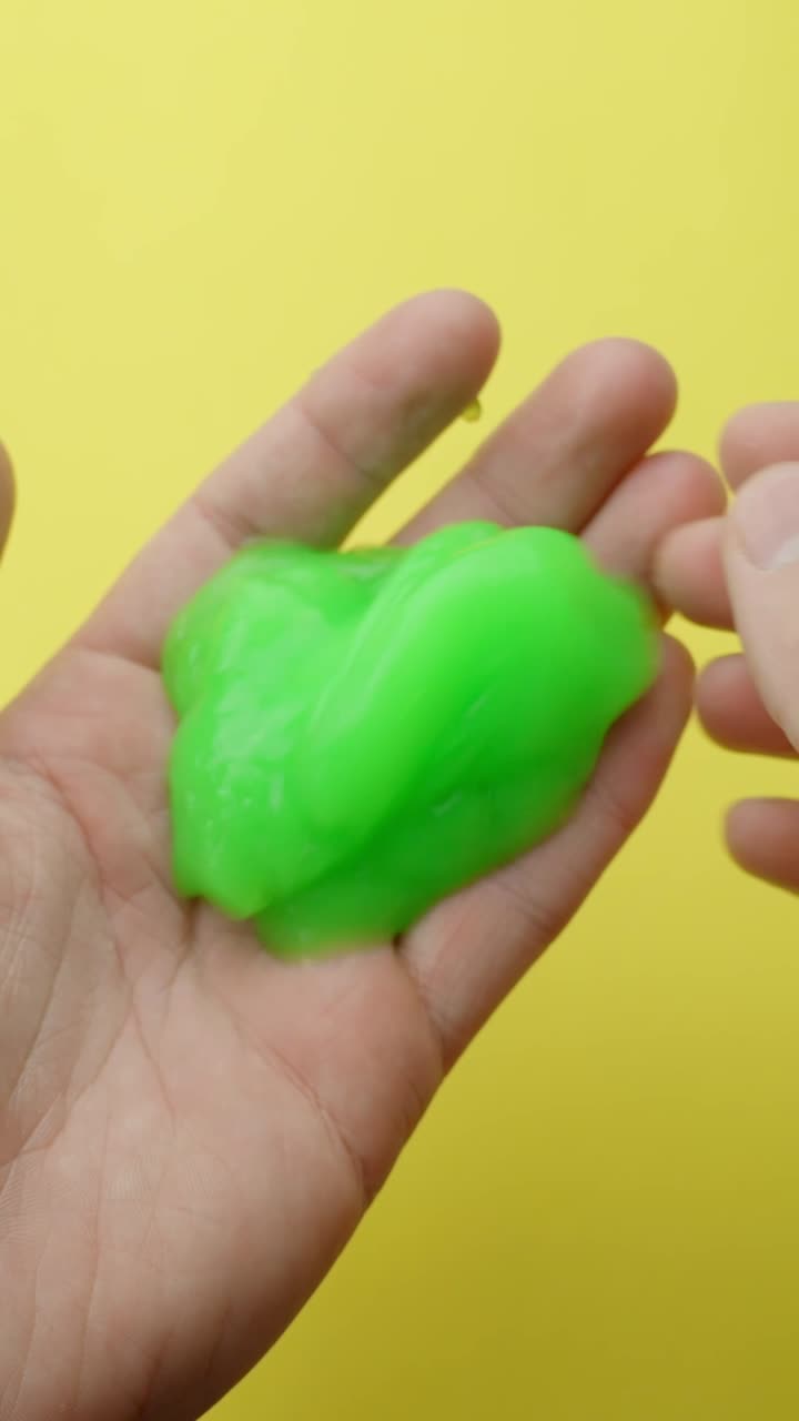 Close-up of green slime being stretched by hands, evokes fun and relaxation, vertical