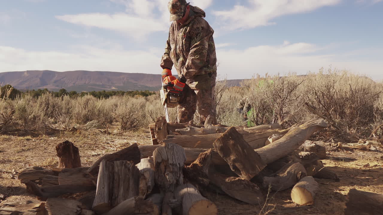 un hombre con equipo de caza usa una motosierra para cortar leña
