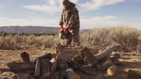 a man in hunting gear uses a chainsaw to cut up firewood