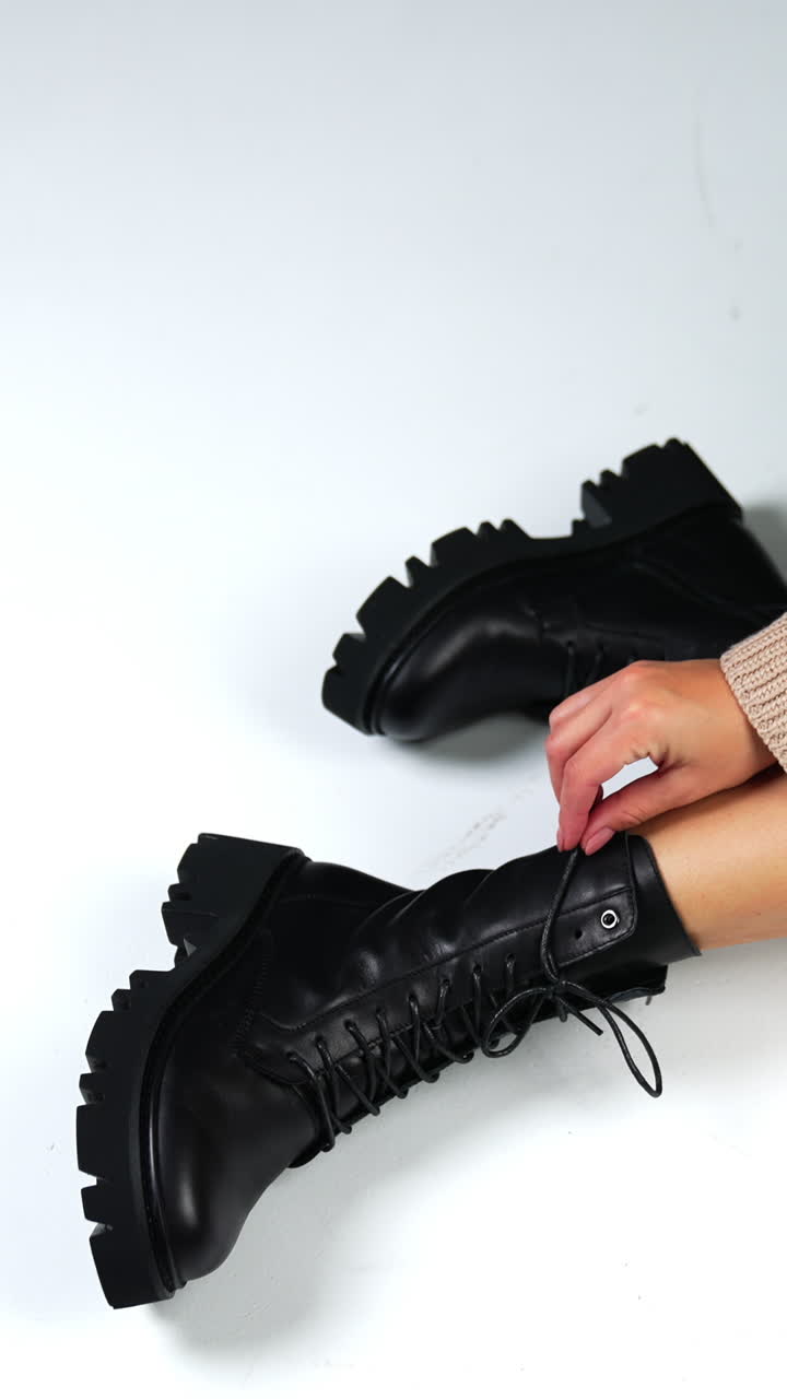 Unrecognized female sitting on the floor in black leather boots with laces. Footwear demonstration. High angle view. Vertical video