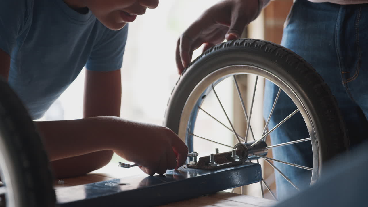 Close up of pre teen boy's hands using a spanner to tighten a nut on the wheel of his go kart, his father helping him, mid section close up