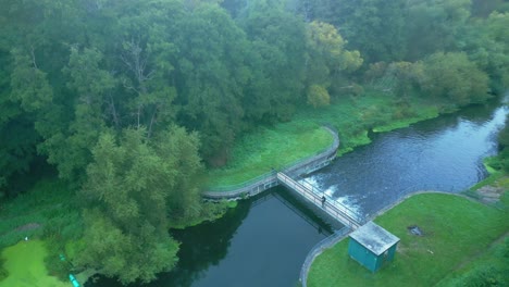 aerial drone view of a person standing over river culvert surrounded by greenery dense nature in sunrise