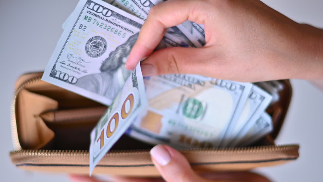 Woman counting one hundred dollar bills in a brown wallet