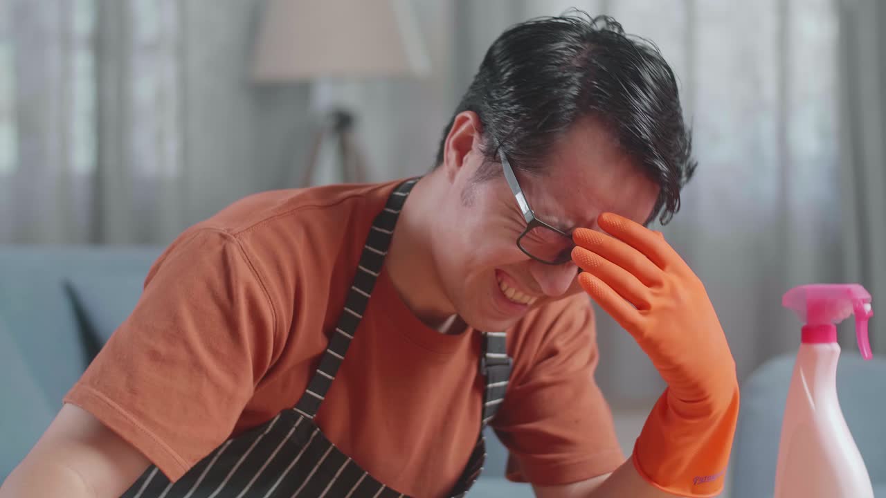 집에서 스프레이로 테이블을 청소하는 동안 울고 있는 아시안 남성 집무원.