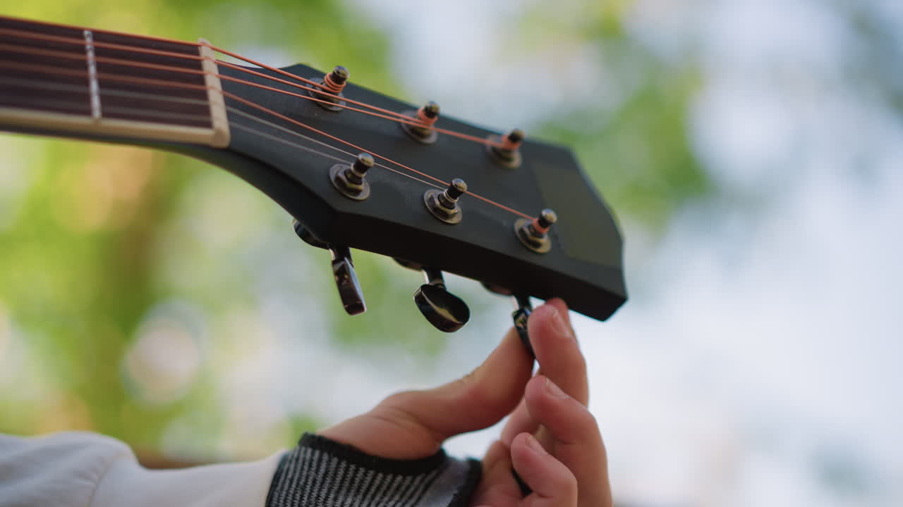 primo piano di mani che accordano una chitarra all'aperto, mano con manica che regola i piroli della paletta nella luce soffusa del sole con sfondo bokeh, momento di prova intimo, precisione delle dita, stato d'animo calmo, texture calda