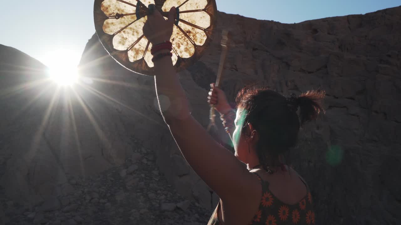 mujer irreconocible tocando la pandereta en el resplandor del sol en las montañas puesta de sol