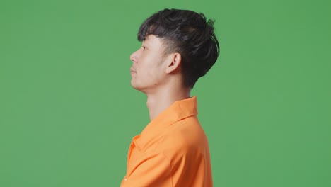 close up side view of asian male prisoner standing on the green screen background, raising head, crossing his arms and looking to camera