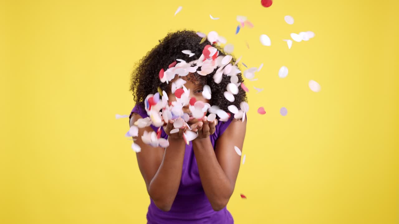 Giovane donna con i capelli ricci che soffia una manciata di oggetti leggeri