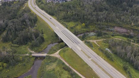 Aerial-hold-over-highway-bridge-at-a-countryside-by-a-park-with-a-romantic-bridge-park-with-paths-leading-to-a-stream-with-perfectly-manicured-lawns-on-a-lush-green-summer-day