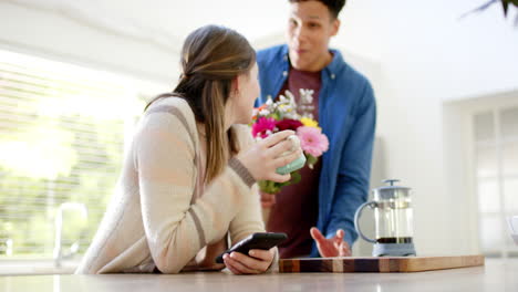 Happy-diverse-couple-giving-flowers-in-kitchen-at-home,-in-slow-motion