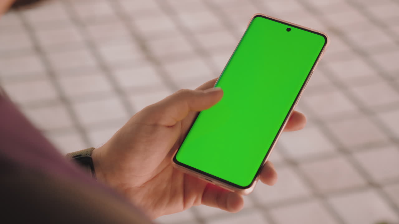 scatto a 10 bit con le mani di un uomo che sblocca e scorre su uno smartphone con schermo verde durante il giorno