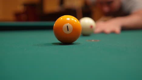 man playing 8 ball pool gets down and shoots solid yellow one ball into pocket past camera using draw or backspin and wooden cue stick on a brunswick table with green felt, playing billiard bar games