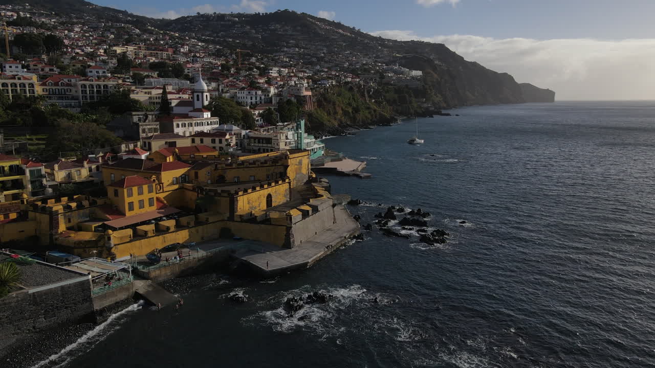 Ripresa aerea che si avvicina al forte di Madeira nella città di Funchal, dove si possono vedere le numerose case e gli edifici sulla costa.