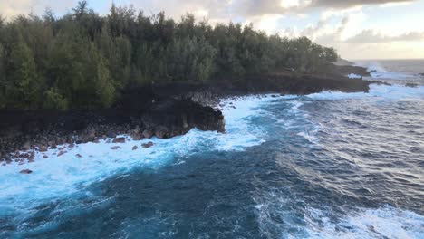 A-drone-gracefully-circles-a-small-cliff-on-the-Big-Island,-Hawaii,-capturing-the-serene-beauty-as-deep-blue-waves-gently-caress-the-rugged-shoreline