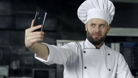 professional chef posing at kitchen. chef making selfie photo with mobile phone