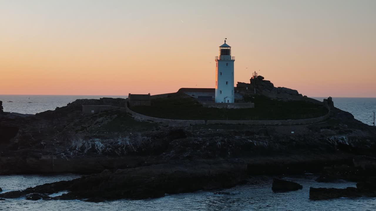 Drone ascends toward Godfrey’s Point Lighthouse at dusk, revealing silhouette against glowing sky, establishing backdrop