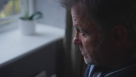 unhappy mature man trying to keep warm by radiator at home during cost of living energy crisis