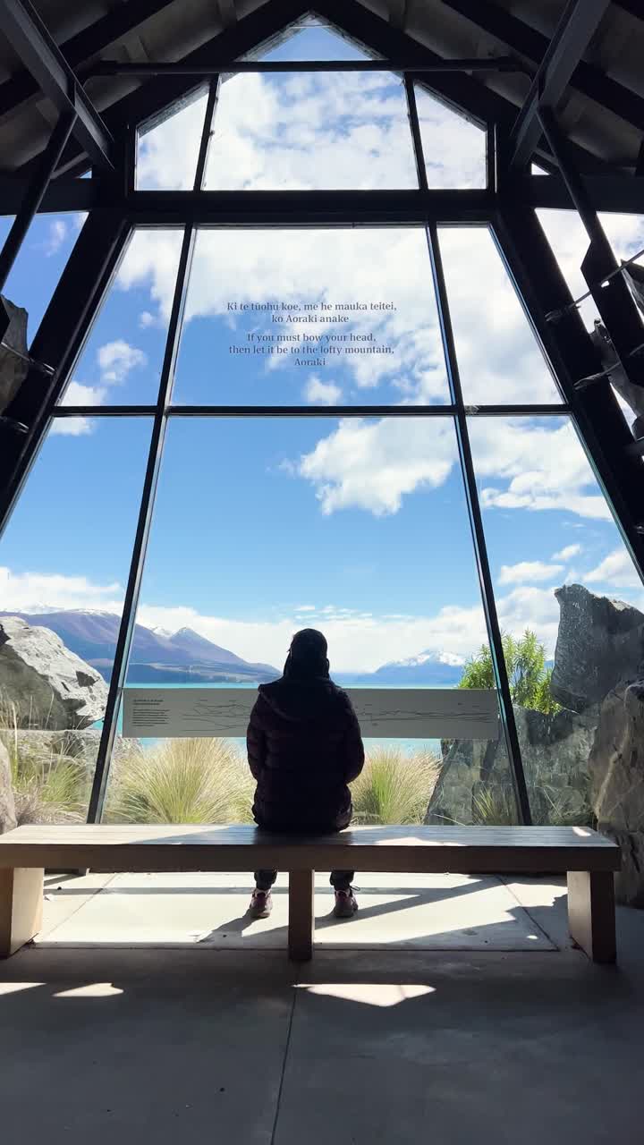 Person rests on bench, stunning Lake Tekapo view fills window, sunny day