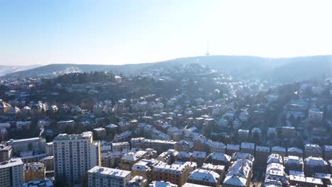 Aerial-top-down-view-tilting-up-revealing-beautiful-city-center-with-red-tile-roofs,-streets-and-mounatins-covered-in-snow-during-winter-in-Stuttgart,-Germany