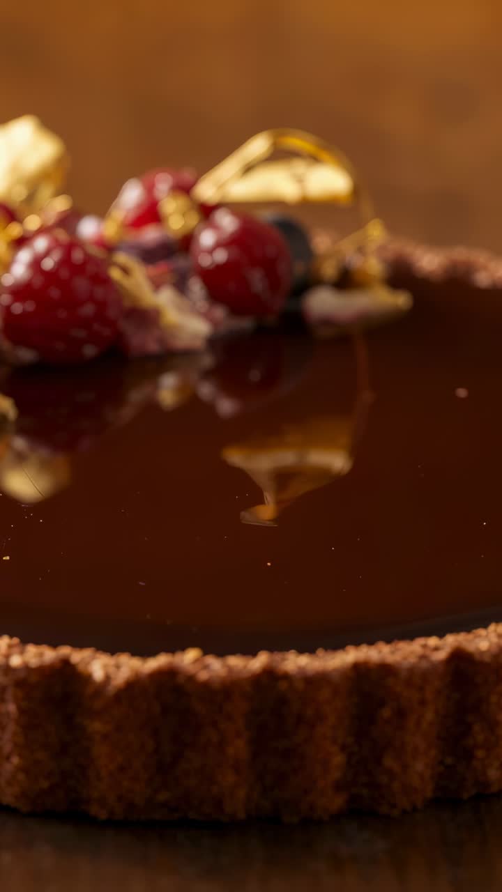 Vertical video: Open frame starting panning camera over chocolate tart at table, revealing berries