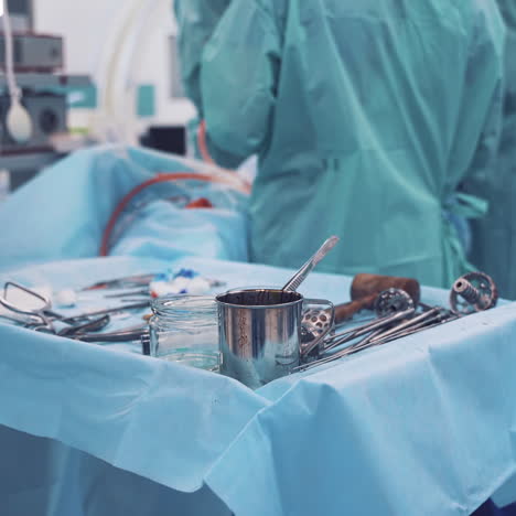 small table covered by blue cloth with medical accessories on the background of surgeons work. operating room with medical team during the operation and different instruments on a table.