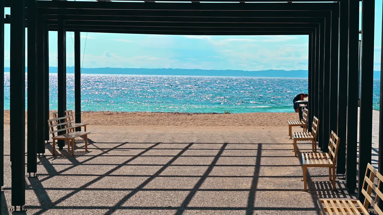 A gazebo on a pier with black metal posts and a benches, Aegean sea in Nikiti, Greece. Slow motion